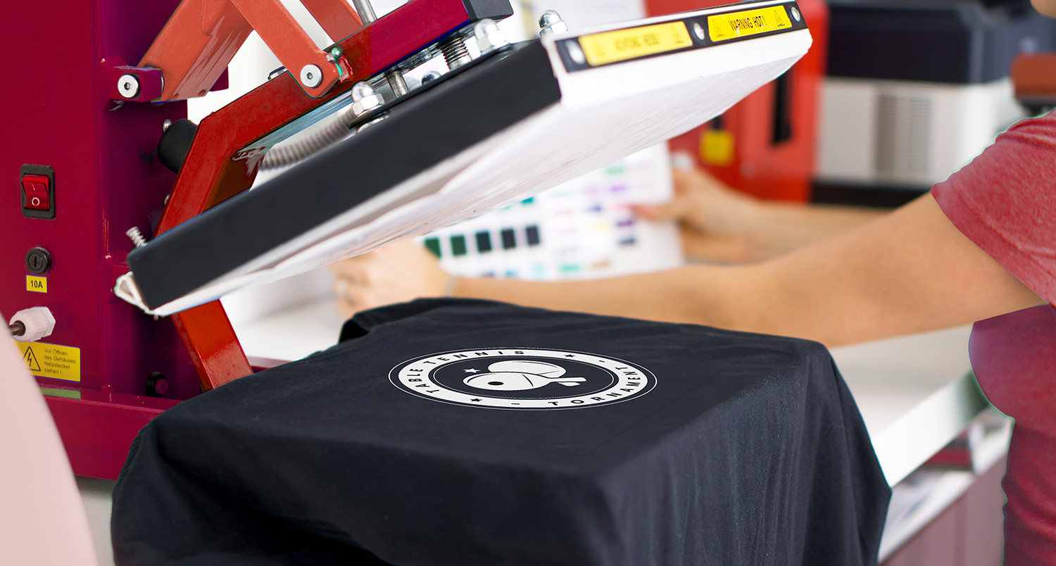 Moderne Transferpresse auf der ein schwarzes T-Shirt liegt welches gerade bedruckt wurde.