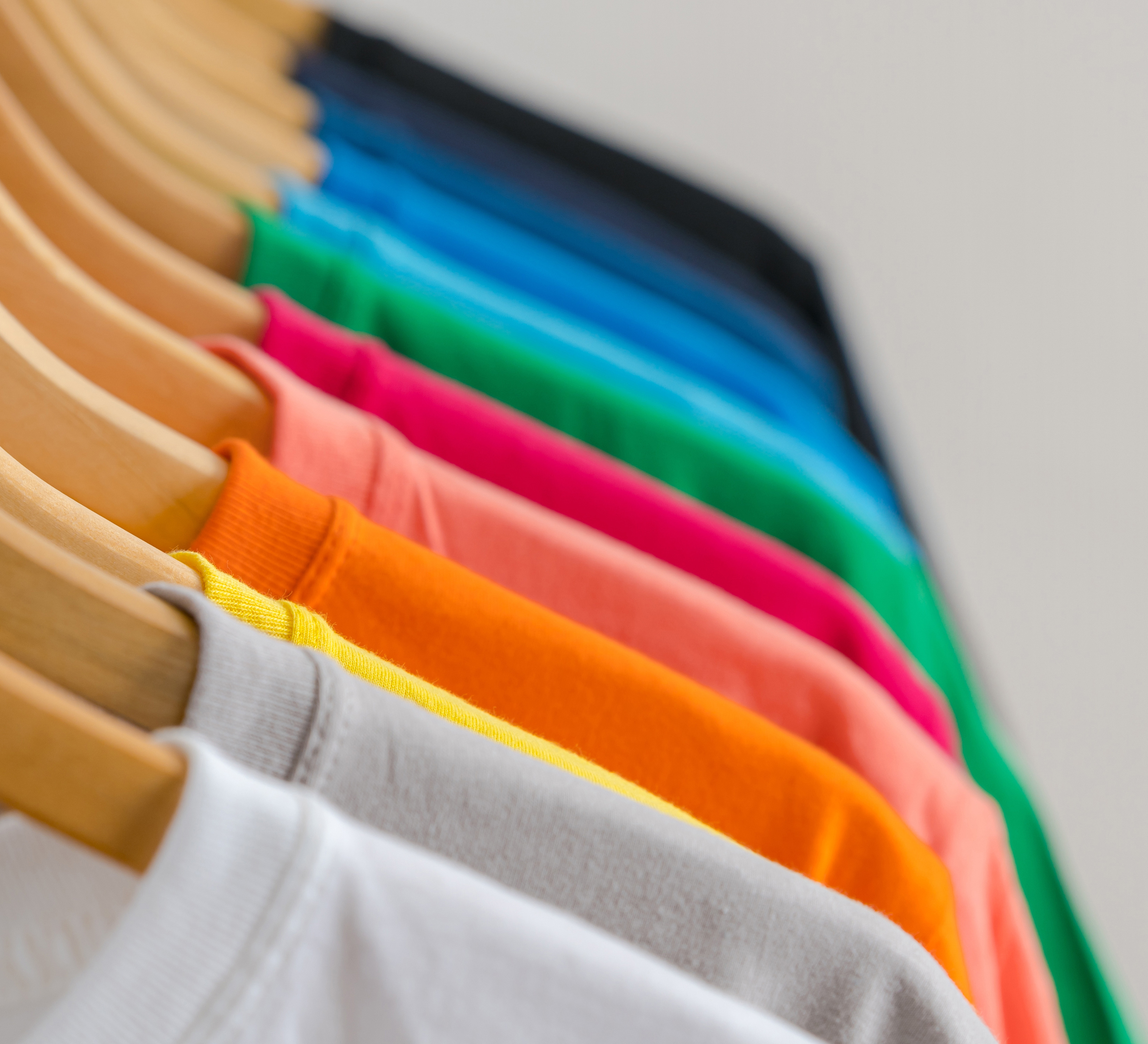 Viele bunter Shirts auf Kleiderhaken an einer Kleiderstange aufgehängt.